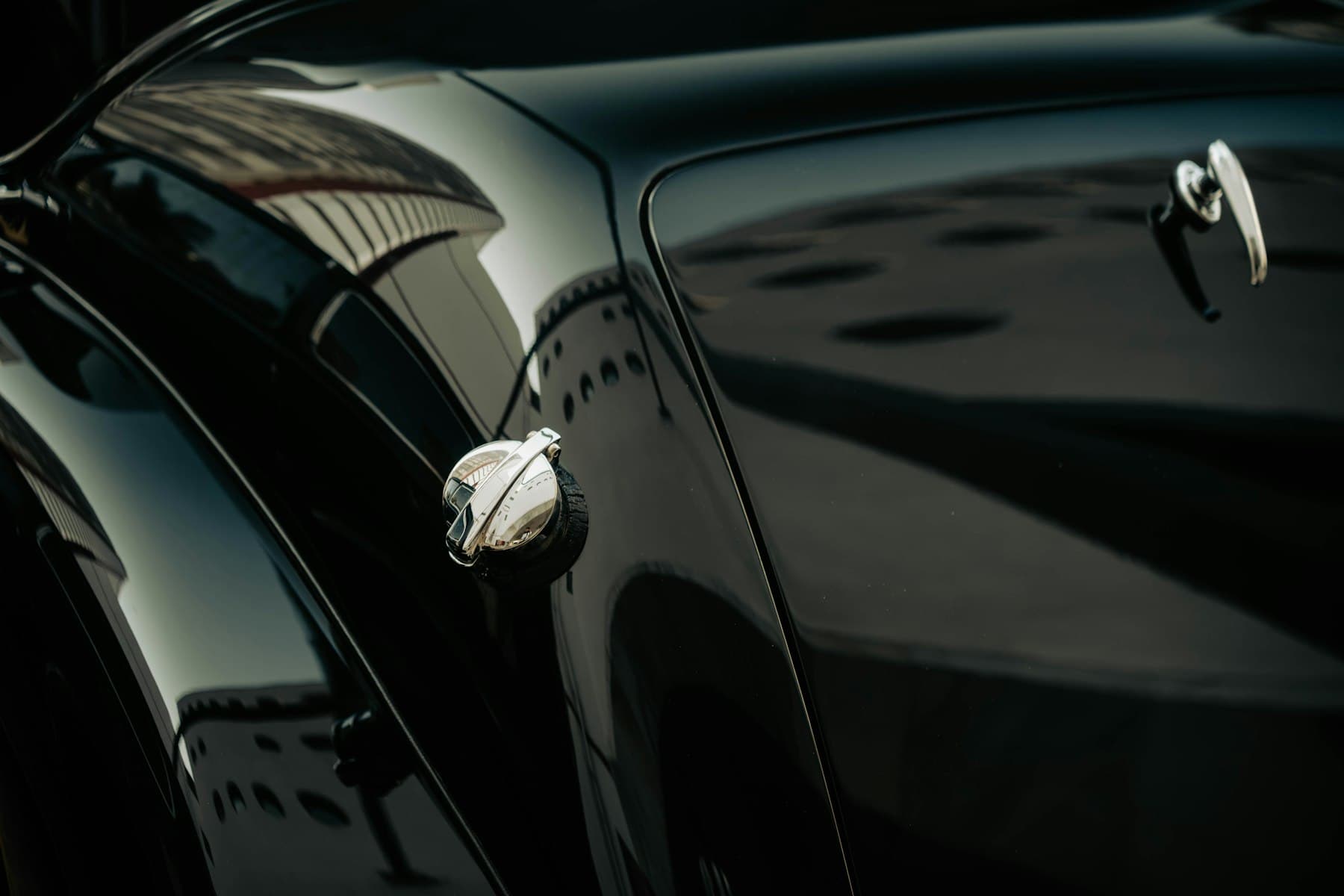 Close-up of deep black paint on a classic car fender reflecting light