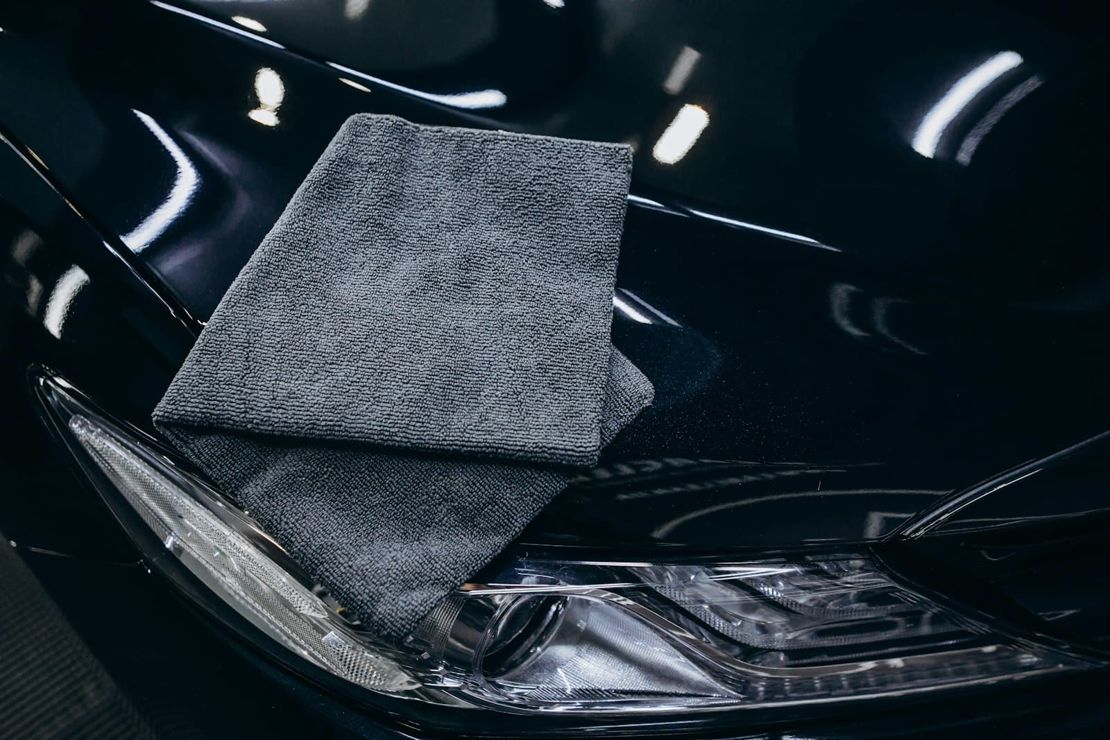 Grey microfiber towel resting on the gloss black hood of a car